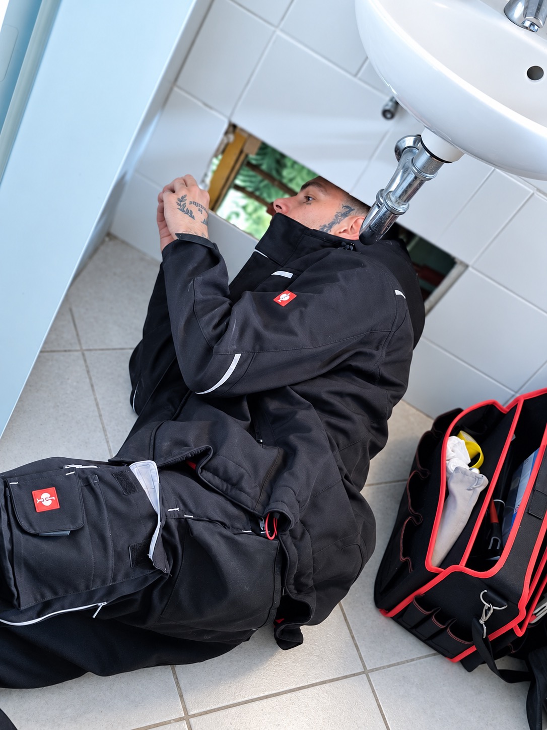 AQORA Monteur arbeitet unter einem Waschbecken an der Sanitärinstallation